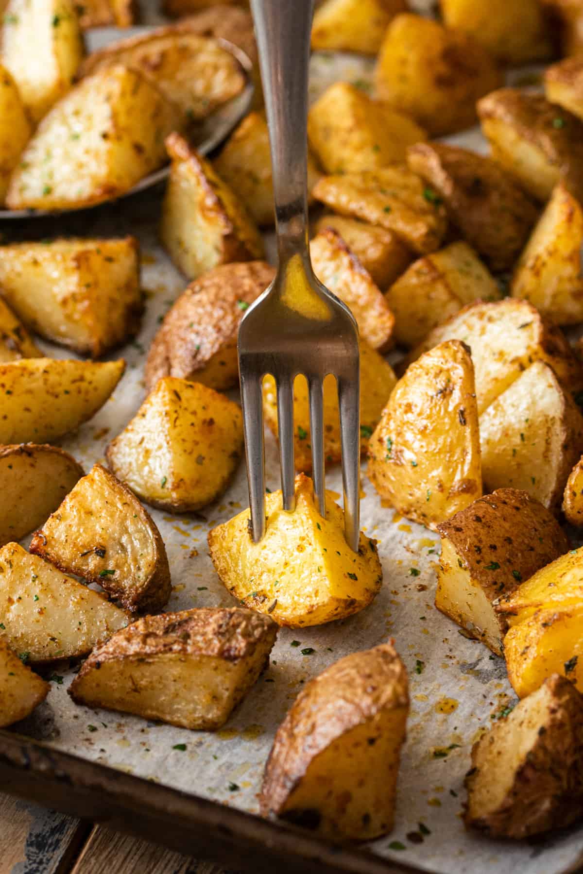 Seasoned oven roasted potatoes baked golden brown on a sheet pan with a fork through one of the wedges.
