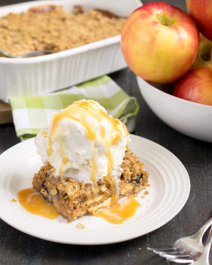 Apple Crisp bars stacked high with caramel dripping of the side and pieces of wax paper between each bar.