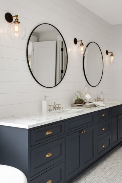 White bathroom with navy vanity, shiplap, and brass fixtures.