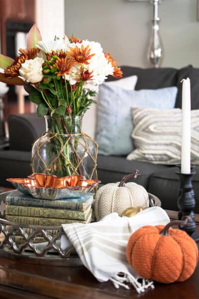 A fall flower arrangement on a coffee table with pumpkins, books, and candlesticks.