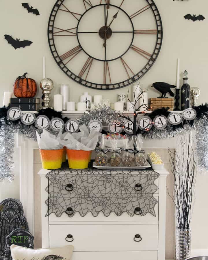 Spooky Halloween mantle with dessert buffet in front. Decorations include ravens, gravestones, a clock, and candles.