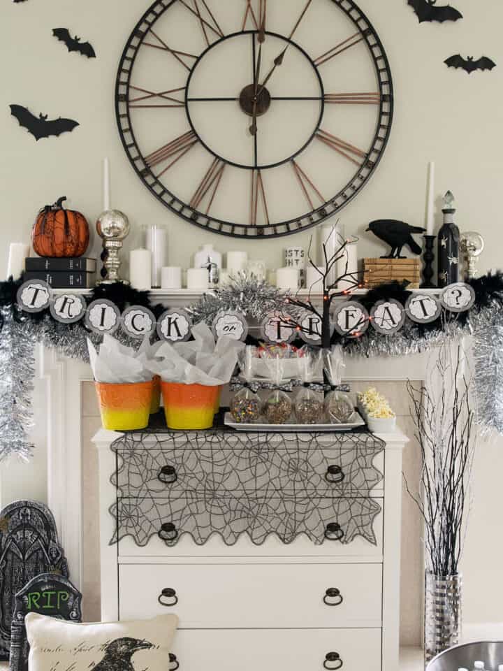Spooky Halloween mantle with dessert buffet in front. Decorations include ravens, gravestones, a clock, and candles.