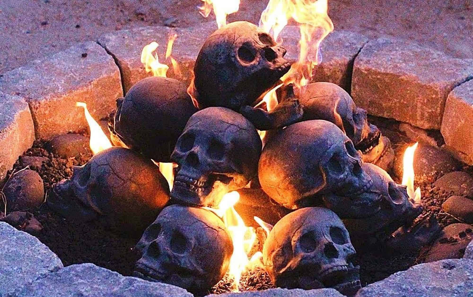 A pile of ceramic skulls in a firepit lit on fire.