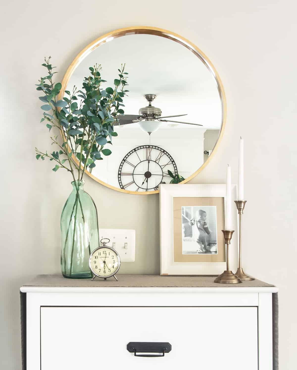 Small dresser decor items including a round mirror, vase, picture frame and candles.