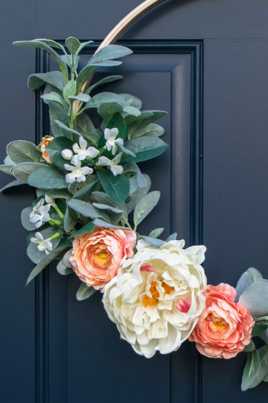 Closeup of a peony spring wreath on a hoop decorating a navy front door.