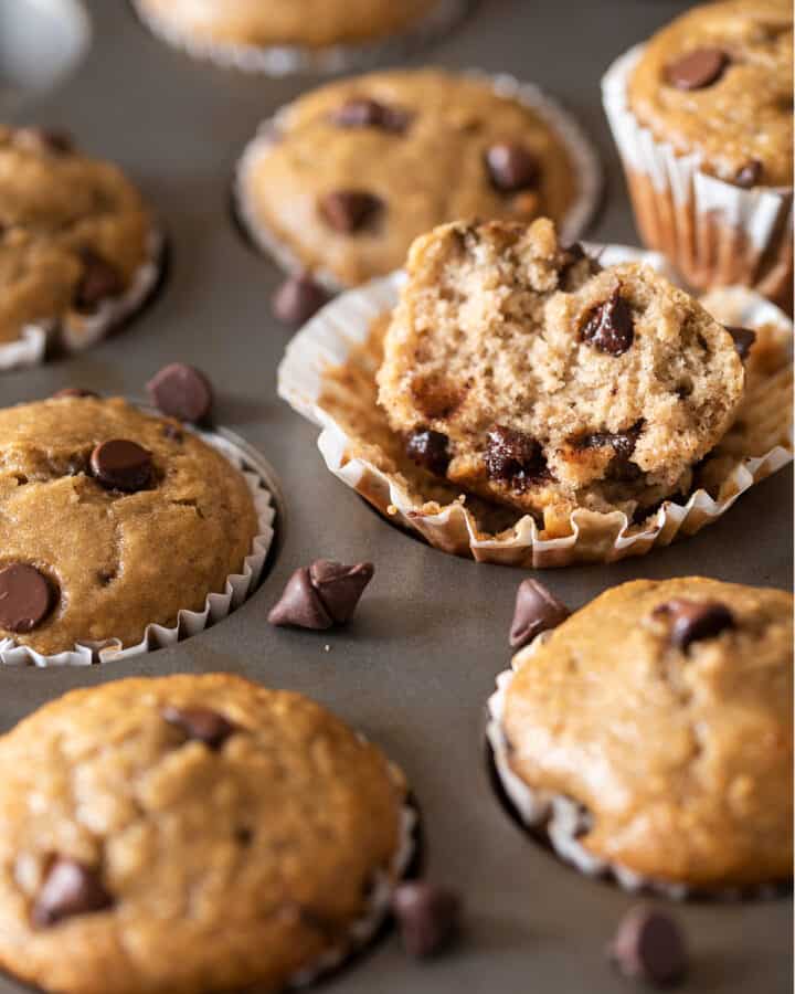 Banana Chocolate chip muffins in a muffin tin with one muffin broken open to show texture.