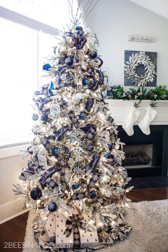 Blue and silver christmas tree that is flocked in front of fireplace.