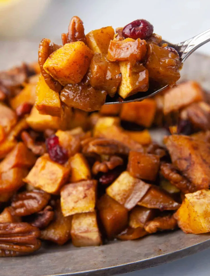 Cubed Butternut Squash with pecans and brown sugar sauce. A spoon is raised up to show texture.