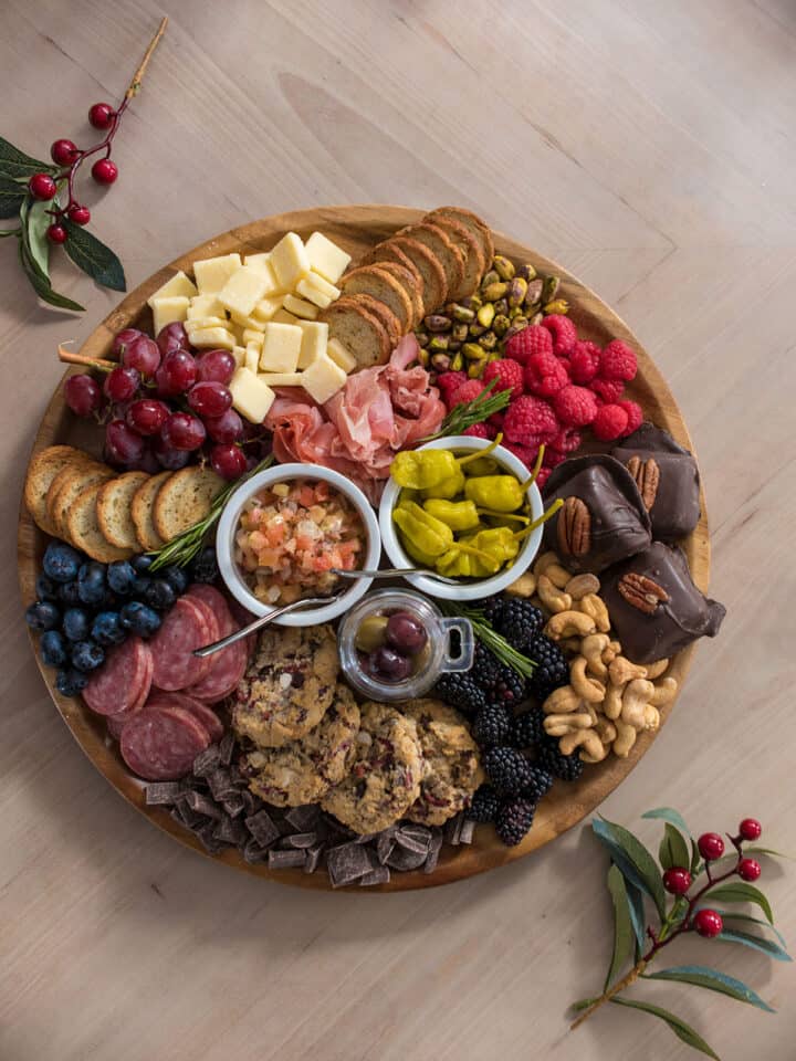 A charcuterie board with cured meats, cheese, and snacks on a wood background.