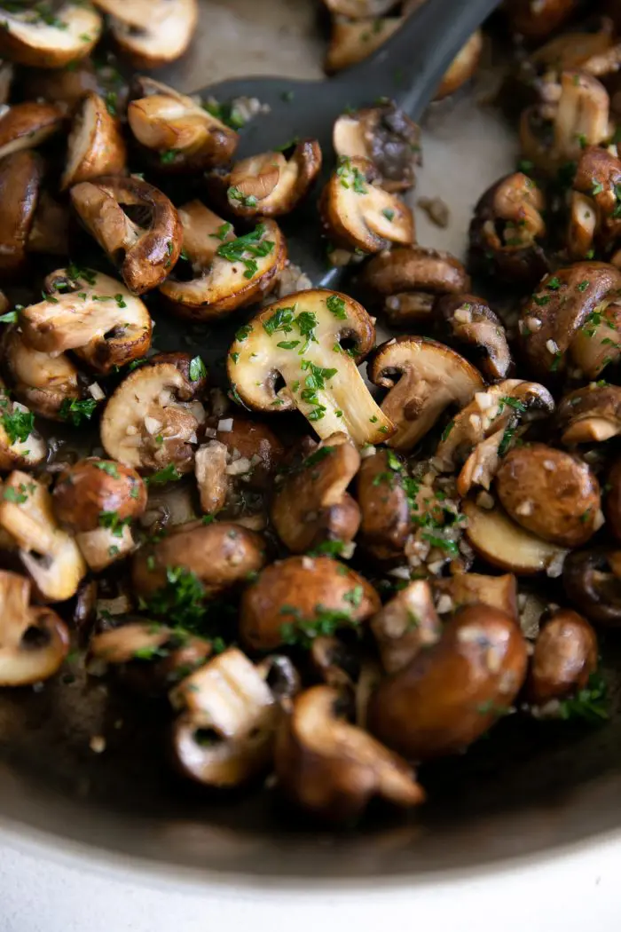 Sautéed mushrooms in a skillet with garlic and parsley on top as garnish.