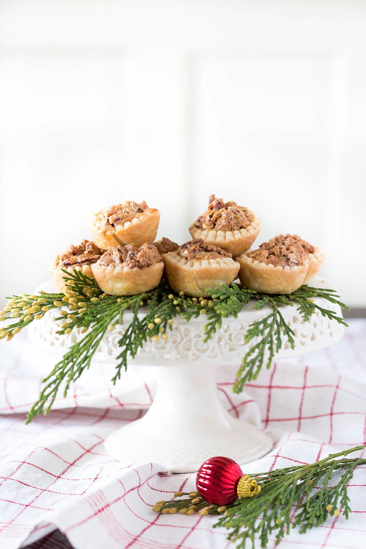 A white cake stand with pecan tassie tarts on top with greenery.