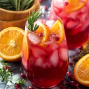 Glass of Christmas Punch garnished with orange slices, pomegranate seeds, and rosemary sprigs.