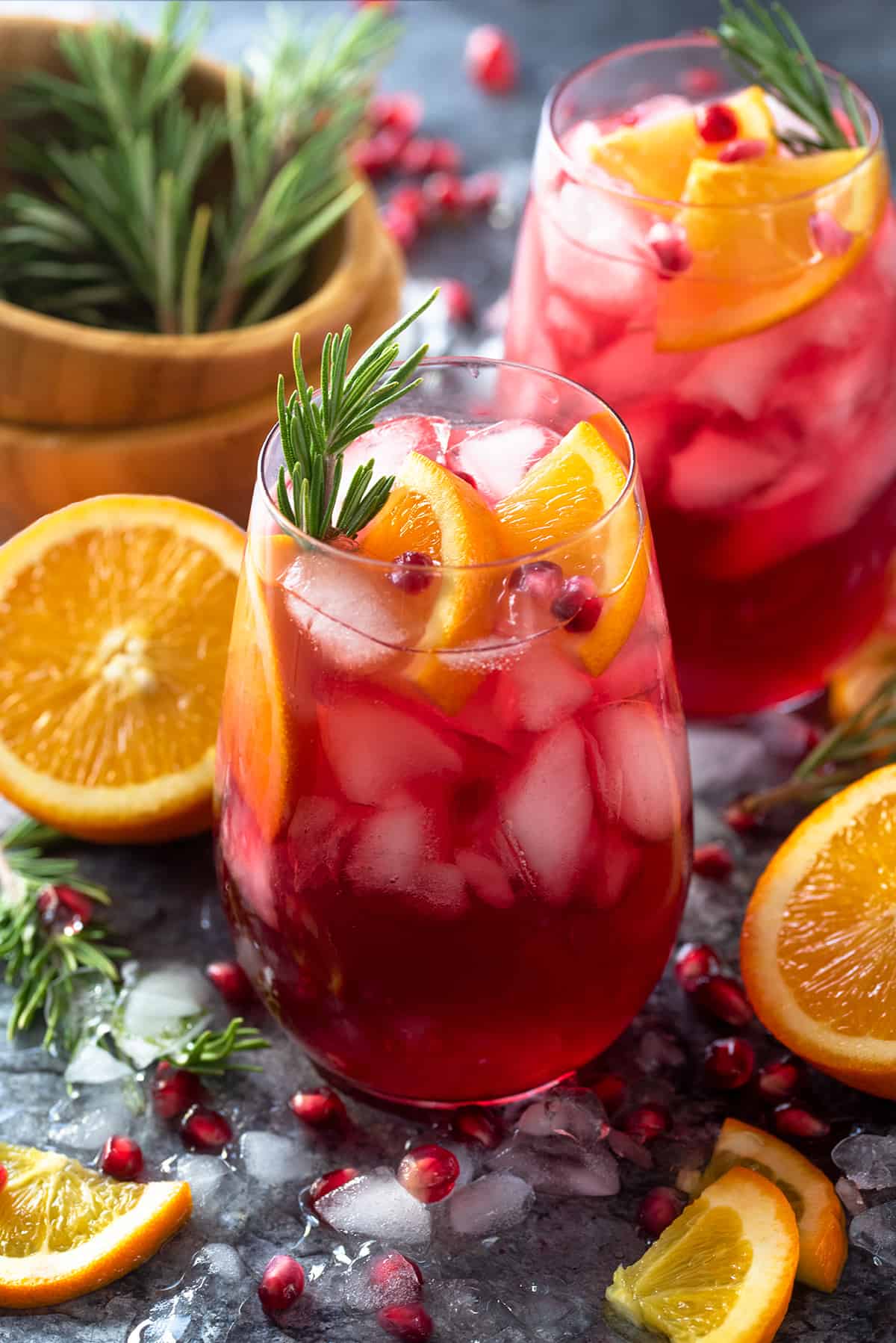 Glass of Christmas Punch garnished with orange slices, pomegranate seeds, and rosemary sprigs.