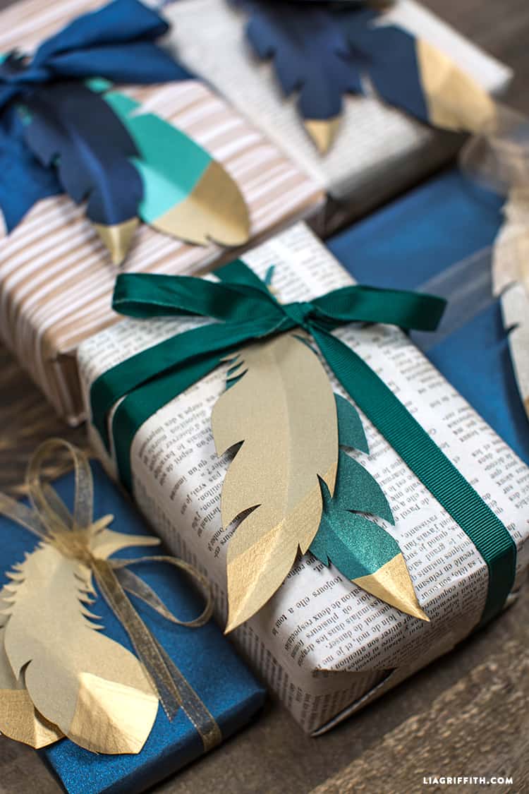 Assorted wrapped packages adorned with paper gold tipped feathers in gold, green and blue hues.