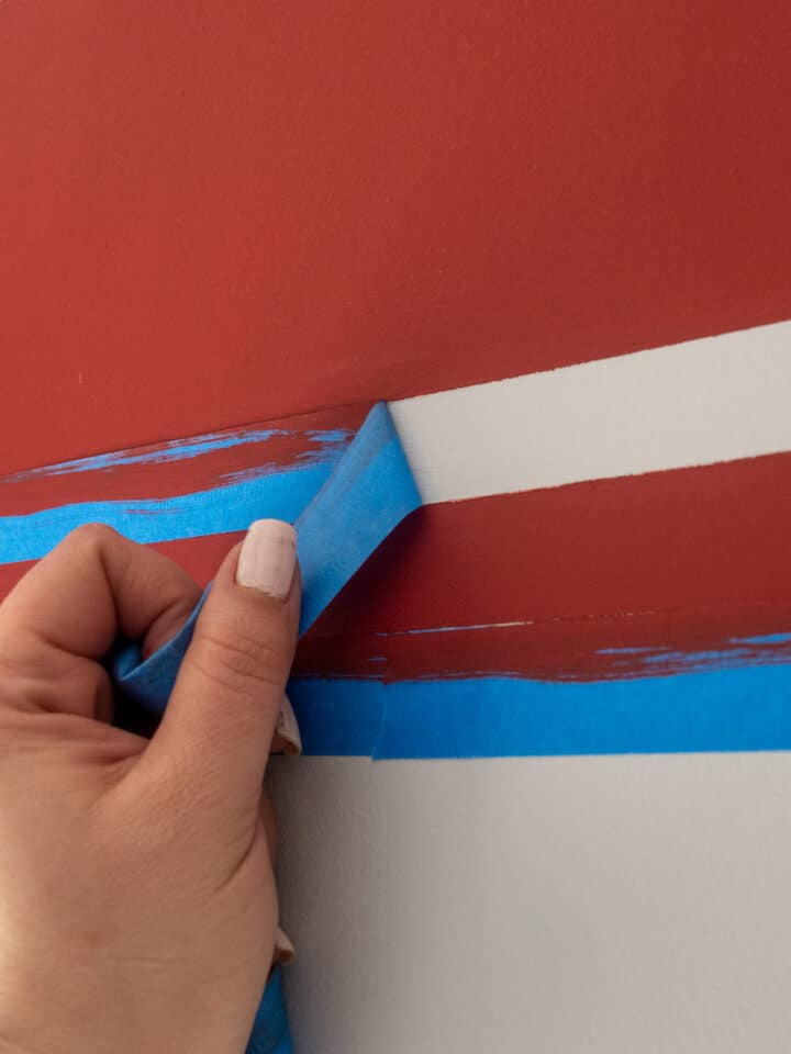 Woman pulling painter's tape away from painted wall for sha4rp lines.