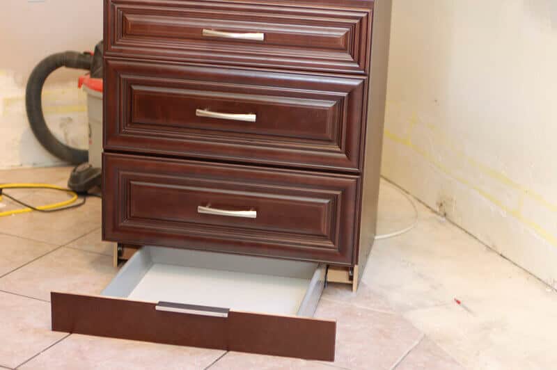 Section of dark wood kitchen cabinetry with slide out secret toe kick drawer.