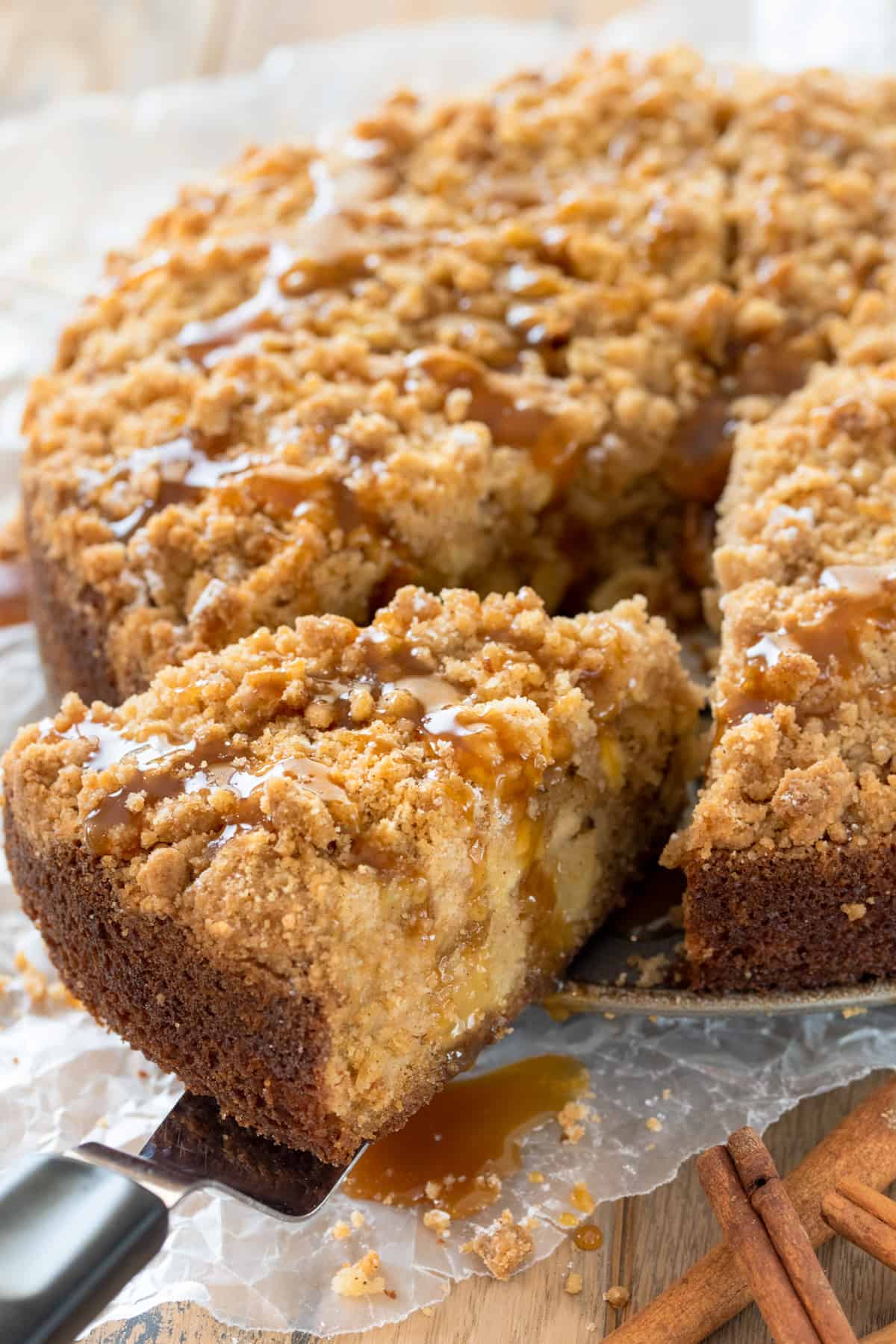 A slice of Apple Crumb cake drizzled with caramel sauce being pulled from a full cake.