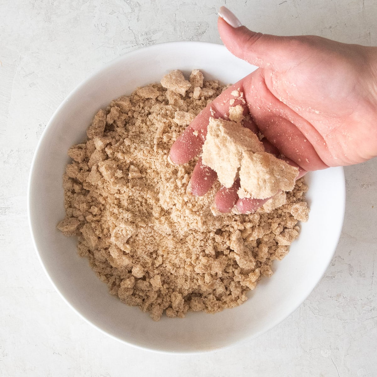 A scoop of crumble topping being squeeze by a hand to show proper texture.