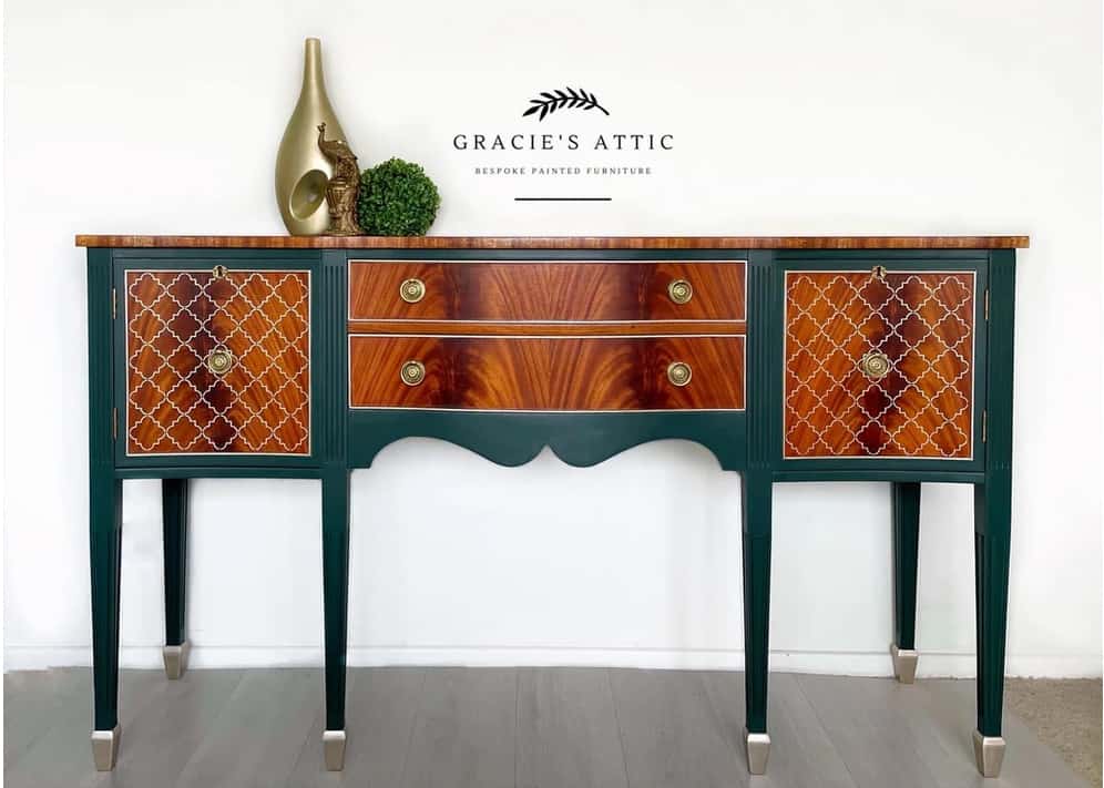 Antique sideboard with dark green accents and dark finished wood drawers fronts and top. Brass hardware and brass decor elements, with a small green topiary.