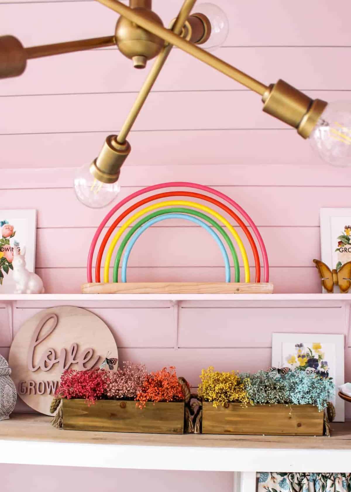 Shelves holding rainbow decorations in front of a pink wall.