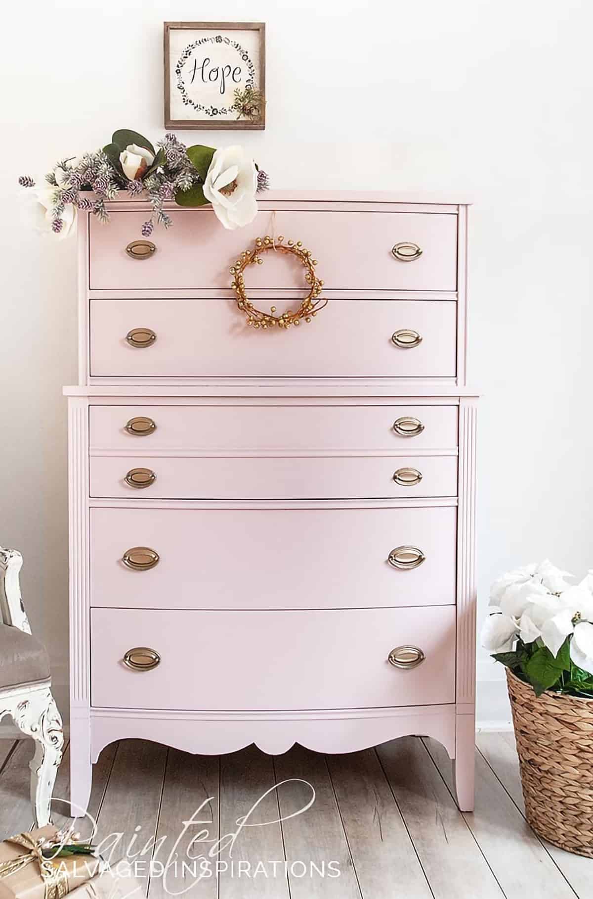 Pink champagne painted chest of drawers with gold pulls surrounded by baskets.