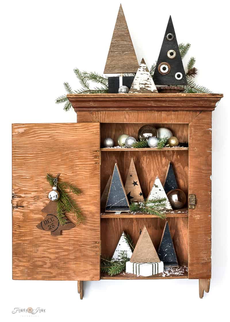 Antique wood cabinet with scrap wood Christmas trees, greenery and metallic ornaments.