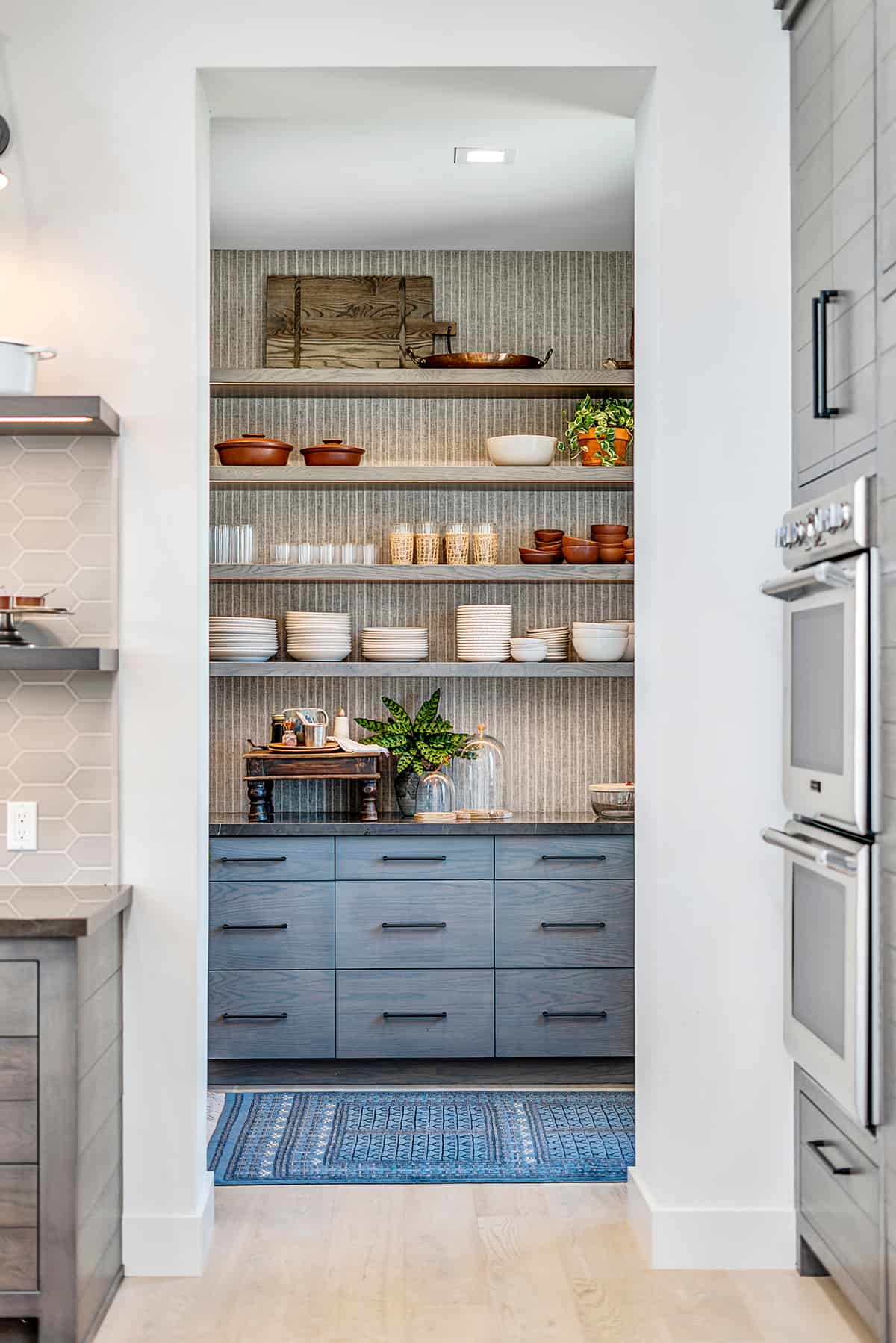 A butler's pantry nook turned with open shelving and blue cabinets. Shelves hold dishes and cookware.