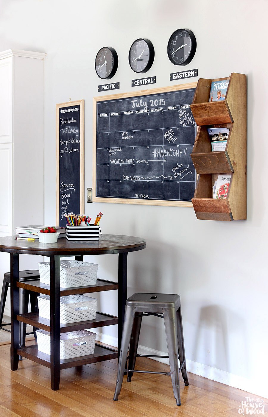 Black chalkboards with scrap wood frames on white wall above round table, with time zone clock display. 