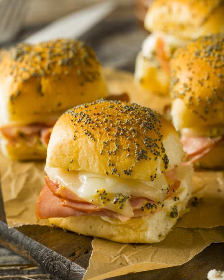 Closeup of Hawaiian roll sliders with ham and cheese on a wood background and wax paper.