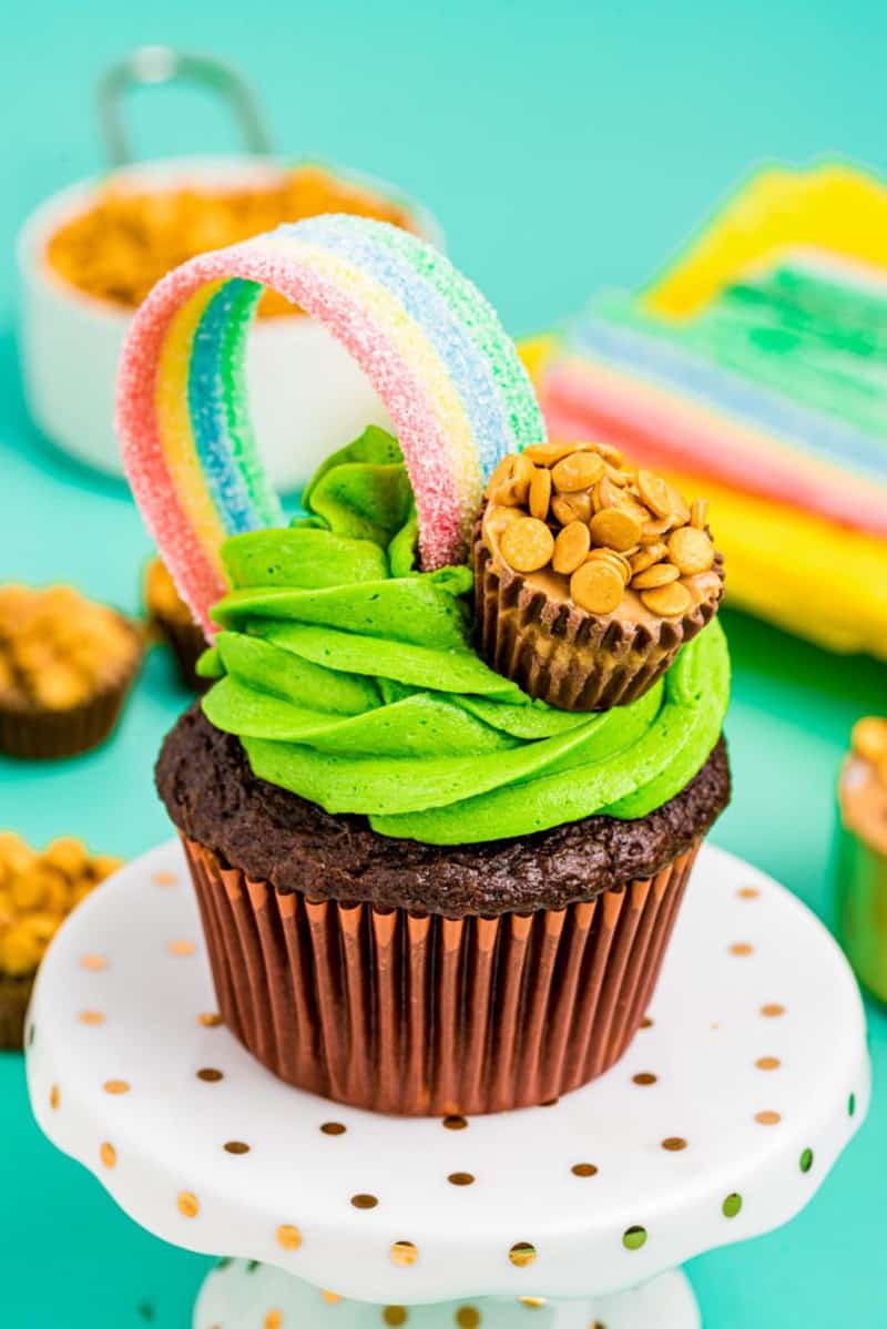 Pot of gold cupcakes made from chocolate cupcake with green frosting and candy rainbow with a Reese's cup pot of gold.