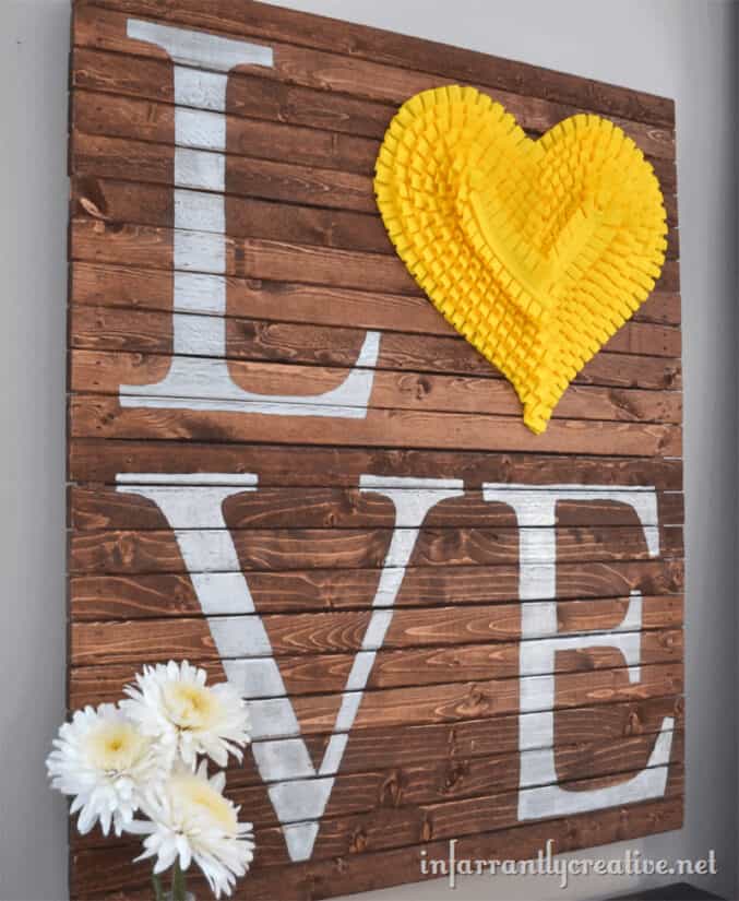 DIY Valentine's Day pallet LOVE art with yellow heart and white painted letters.