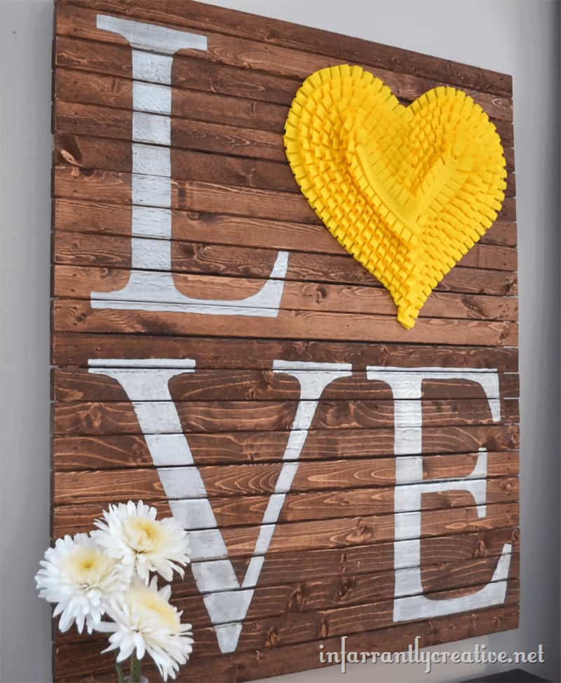Pallet scrap wood wall art piece with Love printed in white paint and large yellow heart detail. 
