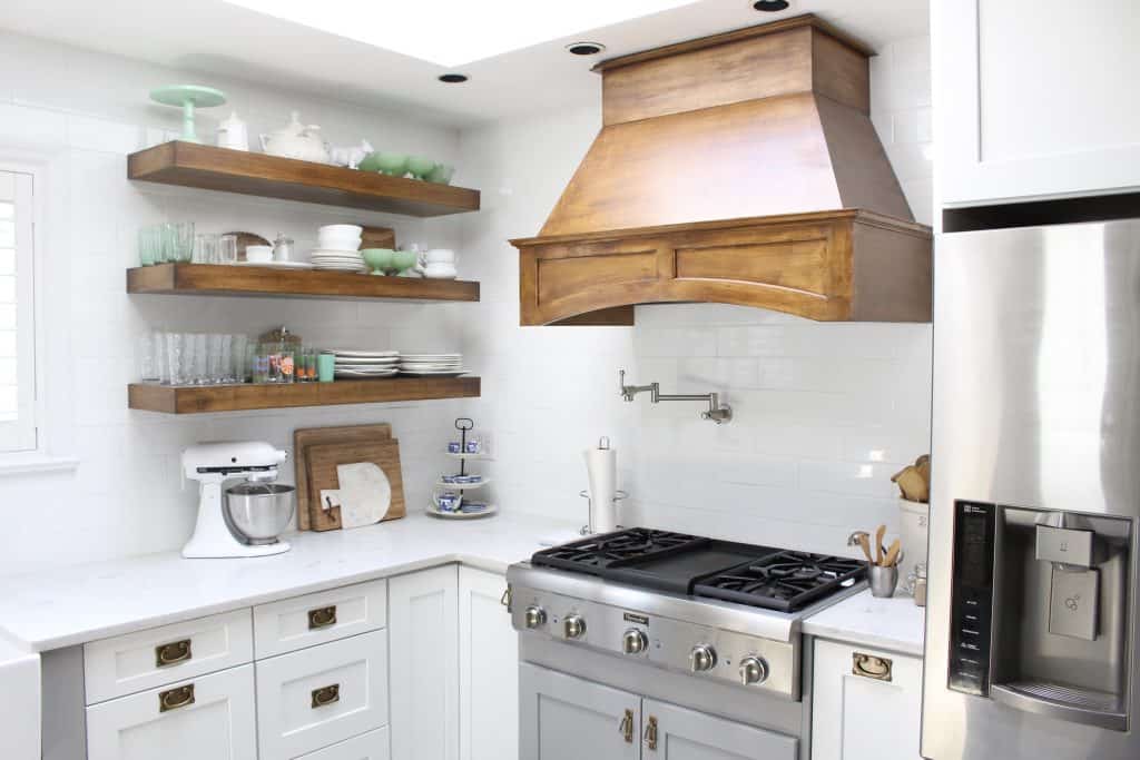White kitchen with open wood shelves and oversized range hood.