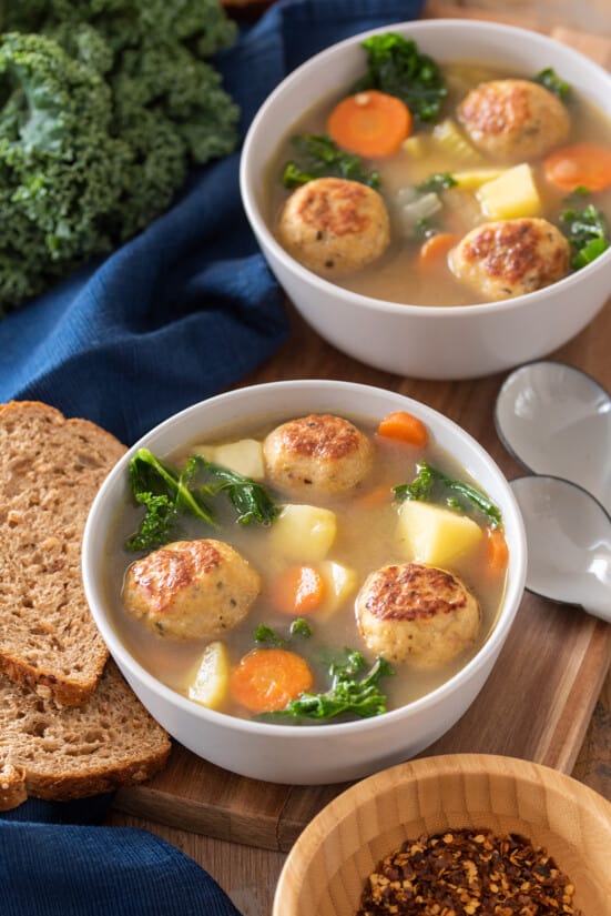 2 bowls of Chicken Meatball Soup with vegetables, carrots, and kale in a broth.