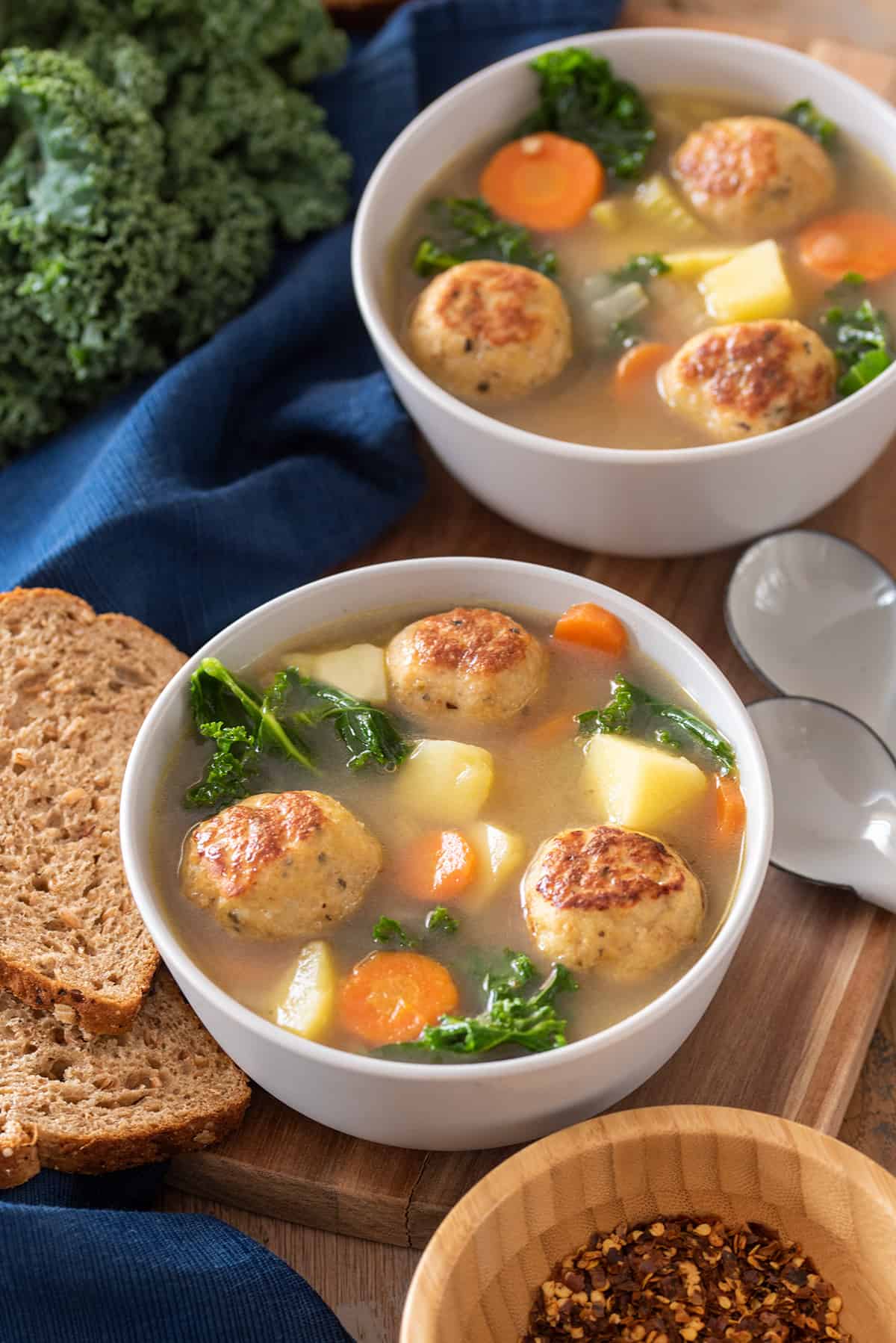 Two bowls of Chicken Meatball Soup with vegetables, carrots, and kale in a broth.