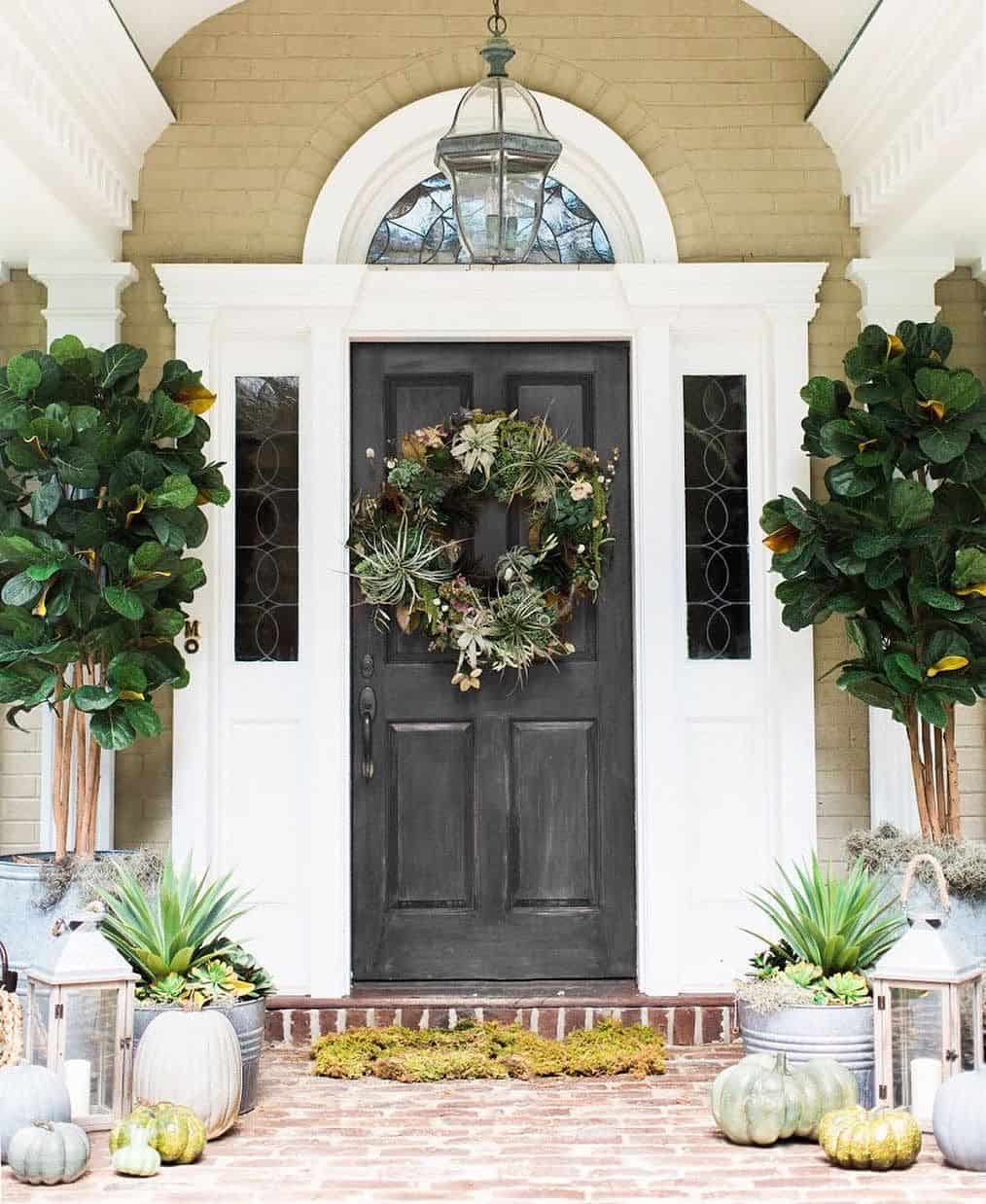Front Porch decor with black door, large trees and plants in pots and brick walls.