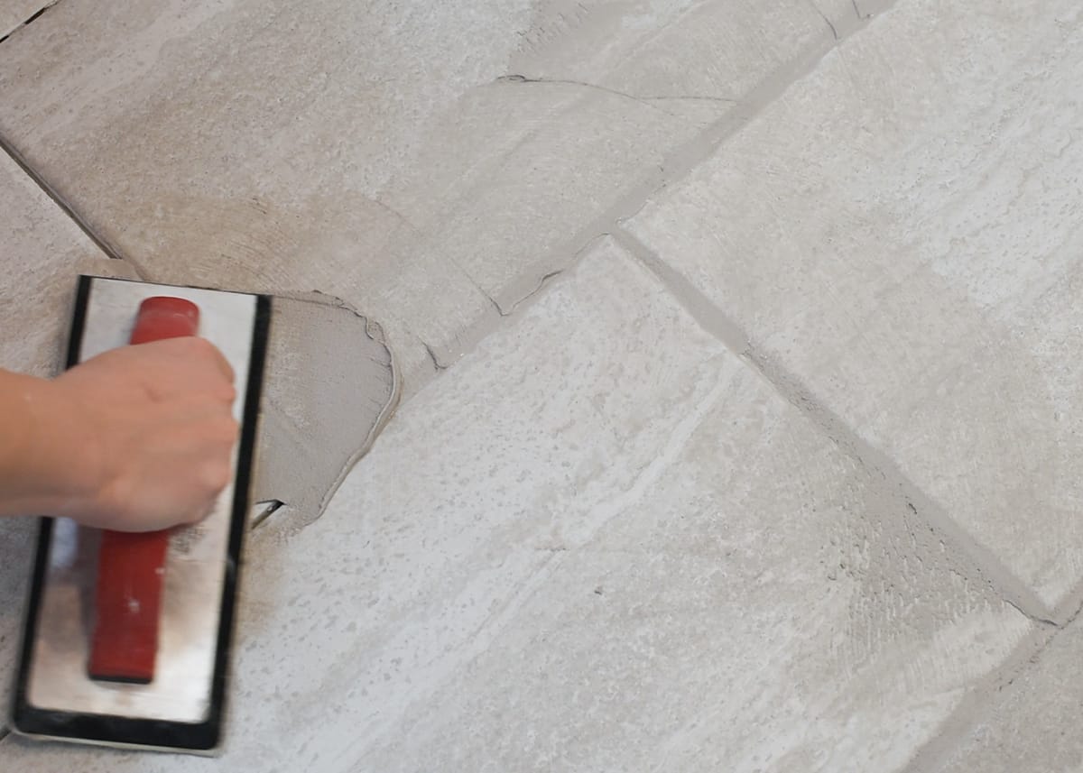 Pushing grout into grout lines of a ceramic tile floor with a rubber float.