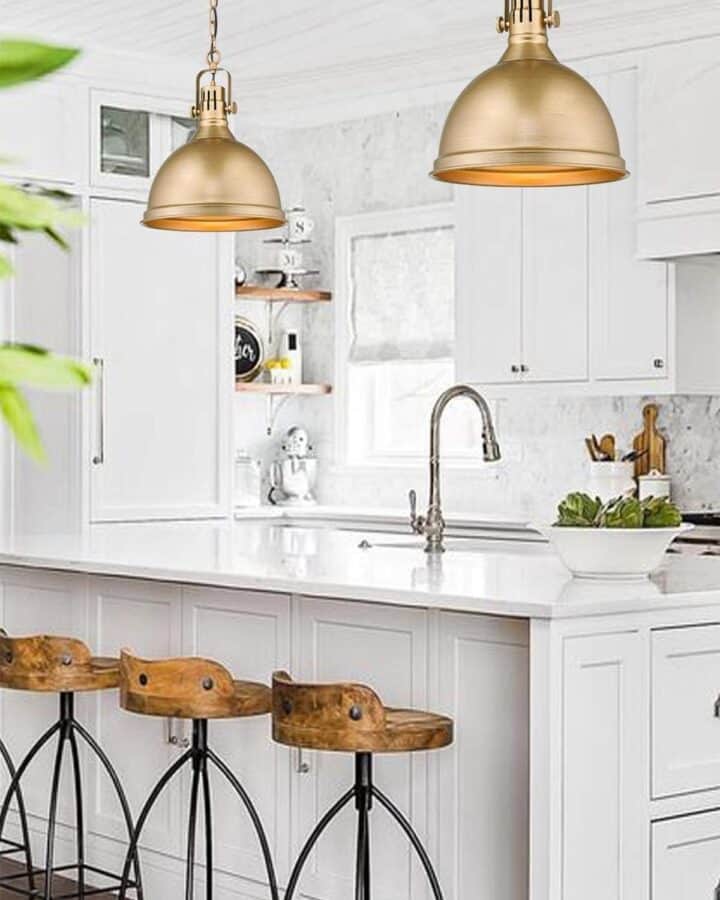 Two large brass bell style pendant lights over white island in modern farmhouse style kitchen.