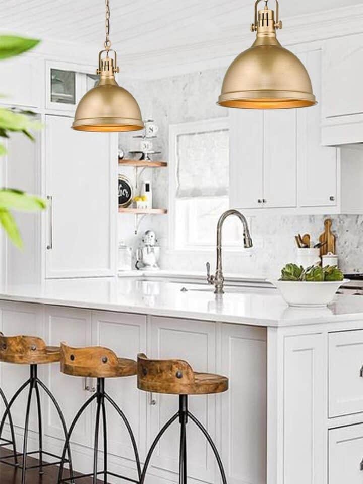 Two large brass bell style pendant lights over white island in modern farmhouse style kitchen.