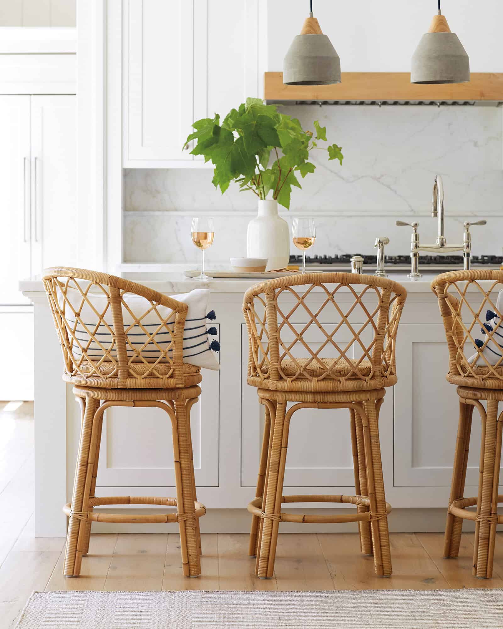 Concrete shaded pendant lights hanging above white island in modern coastal style kitchen with marble backsplash.