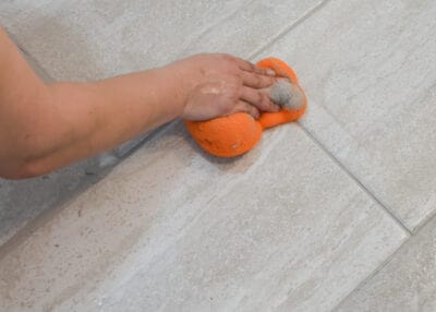 Wiping excess grout off of tile with tile sponge.