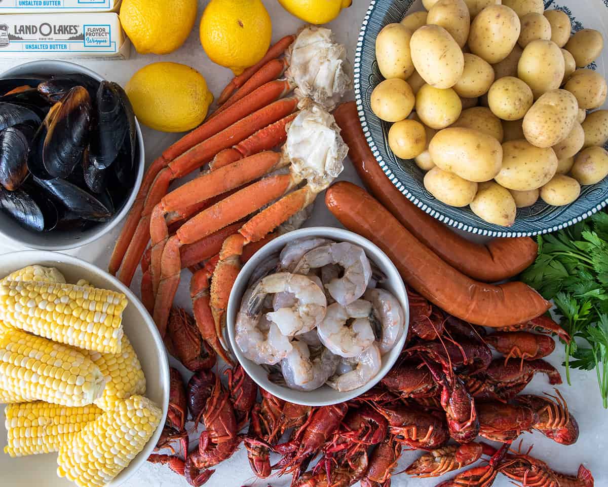 Ingredients for a seafood boil including crab legs, shrimp, crawfish, potatoes and corn.