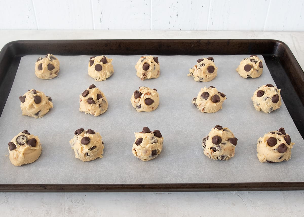 Cookie dough balls laid out on a cookie sheet with parchment paper.
