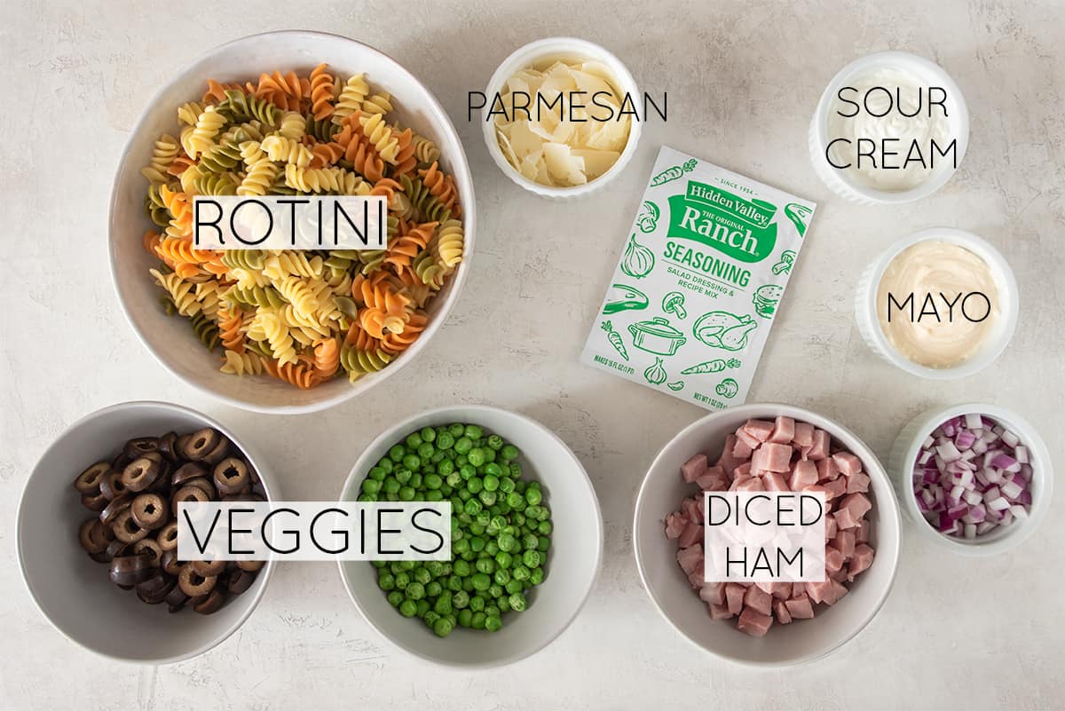 Creamy pasta salad ingredients laid out on a table with text labels.