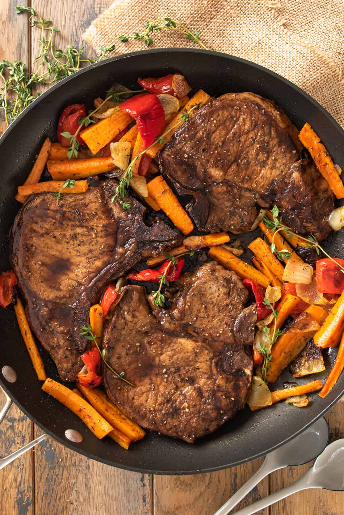 Beefy pan seared pork chops in skillet with vegetables.