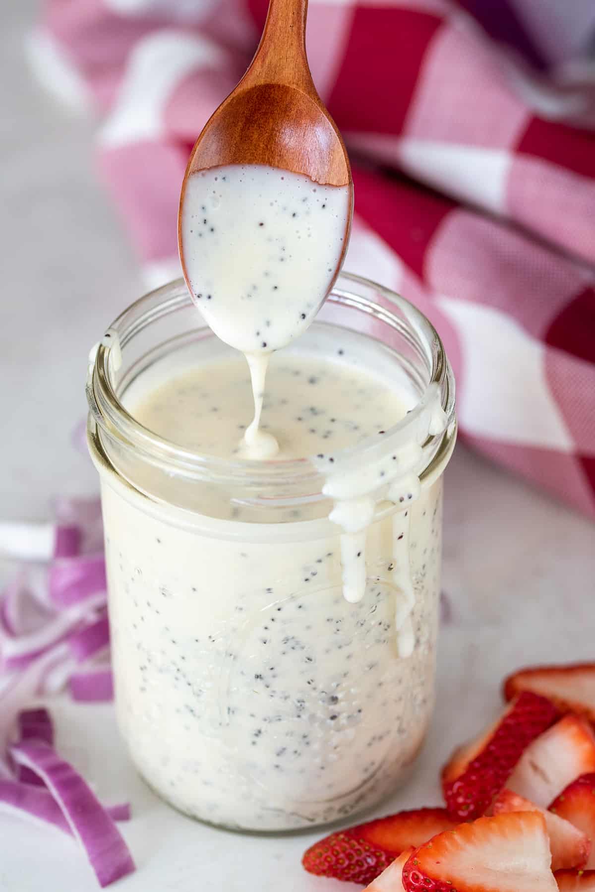 Homemade poppyseed salad dressing recipe pouring from a spoon into a mason jar to show thickness.