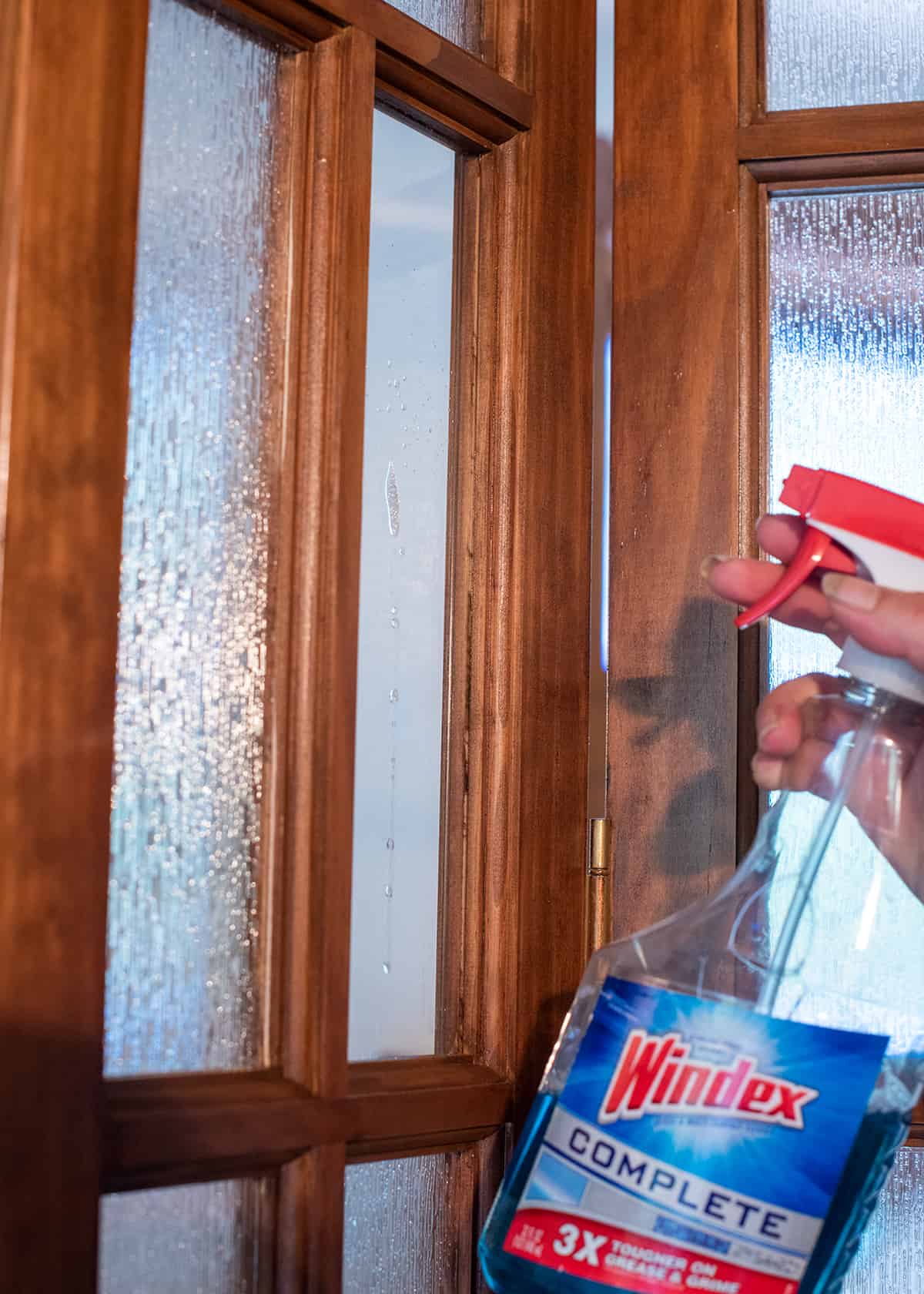 A hand spraying Windex glass cleaner  on a window.