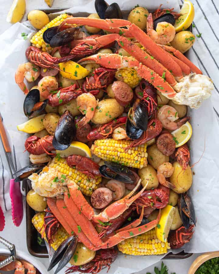 Seafood boil overhead on a table with crab legs, mussels, crawfish, potatoes, corn, and cajun butter sauce.