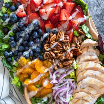 Strawberry Poppyseed salad on a platter with blueberries, mandarin oranges, pecans, red onions, and grilled chicken.