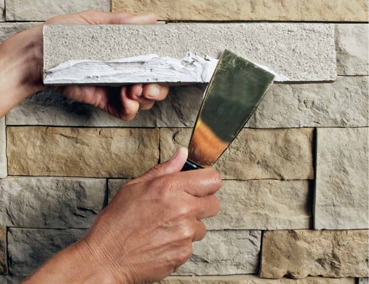 How to spread adhesive on faux stone with a putty knife for installation.